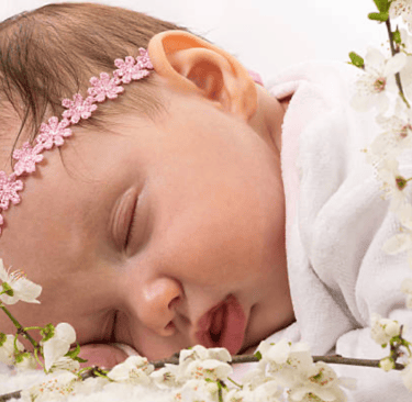 a baby lying on her front, wearing garland of flowers around her head
