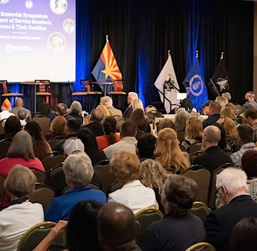 Image shows a crowded room, people in a presenation, watching a speaker ahead of them