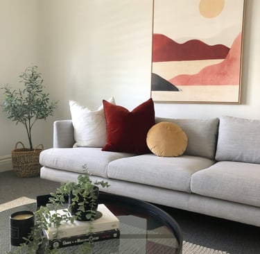 Glass coffee table styled with plant, decorative tray, and books in cozy living room.o