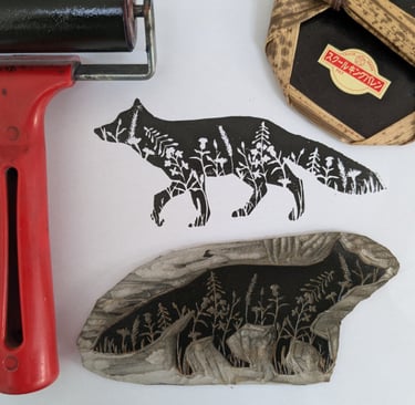 Handmade fox linocut print with floral silhouette detail, carving block, brayer, and baren tool.