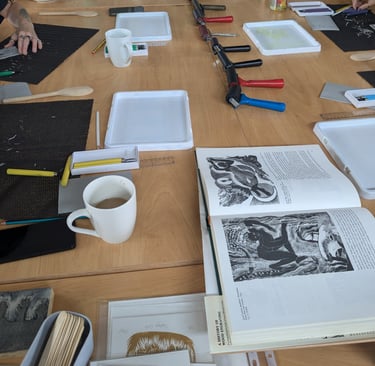 a linocut workshop with all the printmaking tools out on the desk and cups of tea and coffee