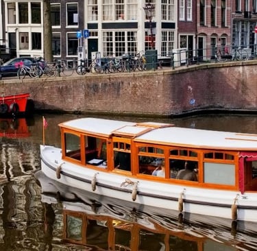A classic wooden canal boat cruising past historic buildings and parked bicycles in Amsterdam.