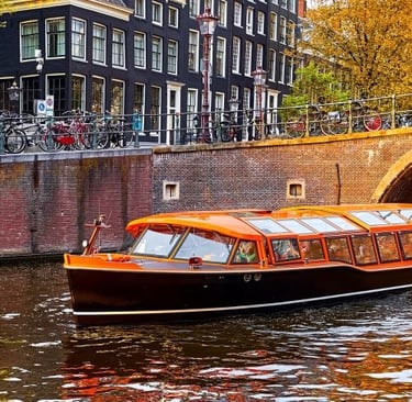 An orange tour boat cruising through an Amsterdam canal past historic buildings and parked bicycles.
