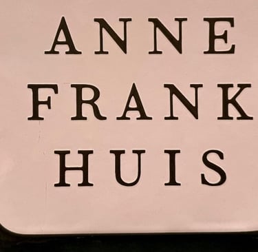 The Anne Frank Huis museum sign in Amsterdam features black serif lettering on a white background.