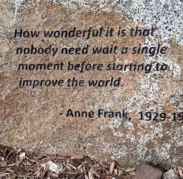 Inspirational Anne Frank quote engraved on a large stone monument over wood chip mulch.