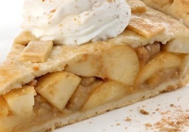 A slice of homemade apple pie with a lattice crust topped with whipped cream and cinnamon.