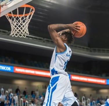Professional basketball player in a white uniform performing a slam dunk at a stadium.