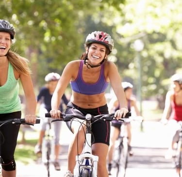 two women riding bikes on a path in a park