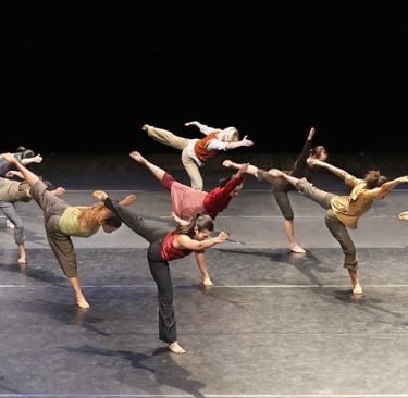 Contemporary dance ensemble performing a synchronized routine with leg extensions on a stage.