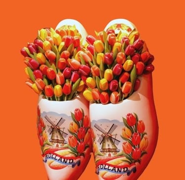 Traditional Dutch white clogs with windmills filled with colorful tulips on an orange background.