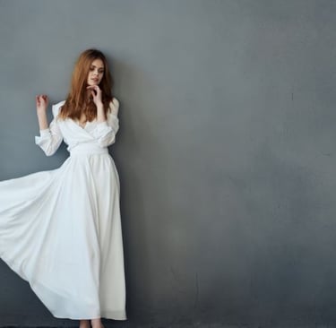 a woman in a white dress standing in front of a gray wall