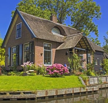 Giethoorn - a house with a thatched roof and a boat on the water