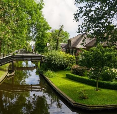 Scenic canal in Giethoorn, Netherlands, with thatched-roof houses and wooden footbridges.