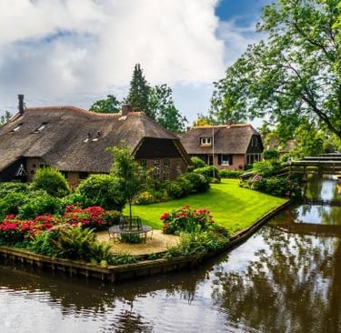 Charming thatched-roof cottages and blooming gardens along a canal in Giethoorn village.
