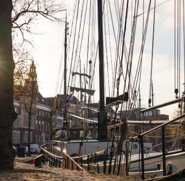 Historic Dutch tall ships with rigging docked in a sunny canal harbor in Groningen, Netherlands.