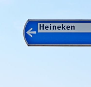 a blue street sign - with heineken on it - an arrow pointing to the left