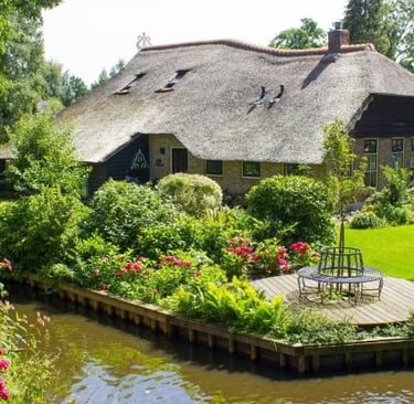 Traditional Dutch thatched roof cottage with a lush flower garden and canal in Giethoorn.