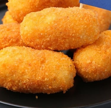 Golden brown crispy potato croquettes served on a black plate, close-up shot.
