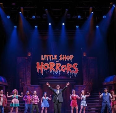 a man in a suit and tie standing on stage with the sign “little horrors”