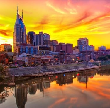 Nashville skyline reflecting in the Cumberland River during a vibrant orange and yellow sunset.