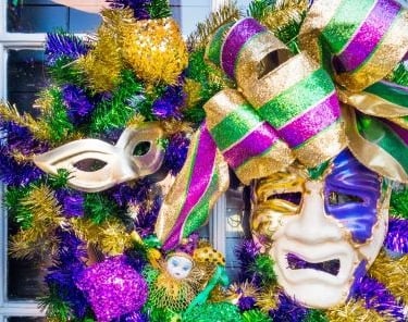 Festive Mardi Gras wreath featuring purple, green, and gold tinsel, ribbons, and theater masks.
