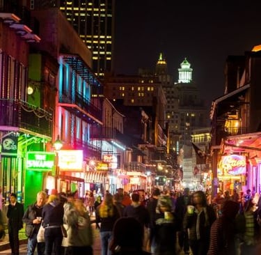 Crowded Bourbon Street at night with bright neon signs and historic French Quarter architecture in New Orleans.
