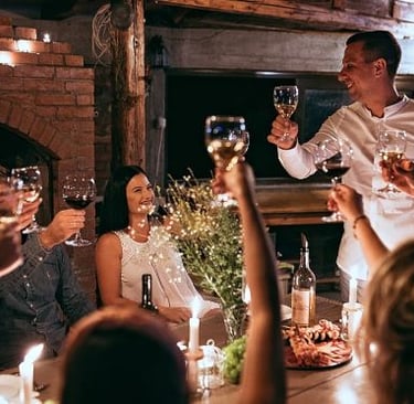 Smiling friends toast with wine glasses during a cozy candlelit dinner party in a rustic cellar.