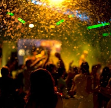 Crowd dancing at a night club party with golden confetti and glowing bokeh lights.