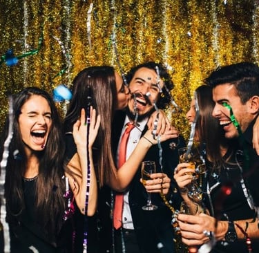 Cheerful friends celebrating at a New Year's Eve party with confetti and gold tinsel background.