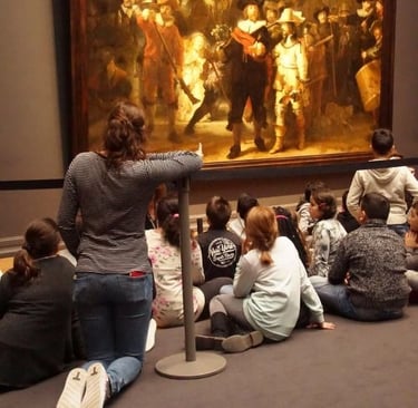 Students in a museum sitting on the floor viewing Rembrandt's Night Watch painting.