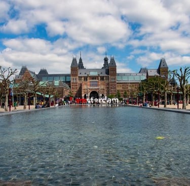 Rijksmuseum building in Amsterdam behind the Museumplein water pond on a sunny day.