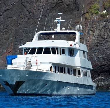 Luxury white yacht cruising past volcanic cliffs on a blue ocean excursion.
