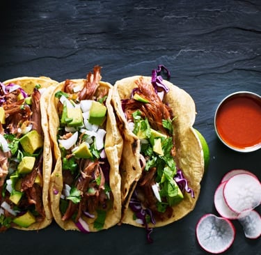 a group of three tacos with a bowl of sauce and a bowl of sauce
