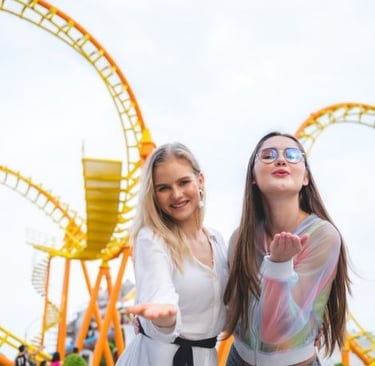 two women standing next to each other in front of a roller coaster
