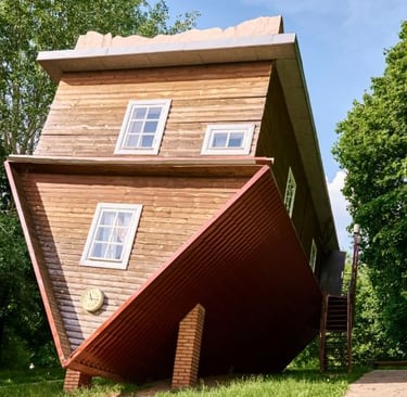 A wooden upside-down house tourist attraction standing on its roof in a green park.