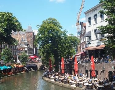a river with people sitting at tables close to a canal in utrecht