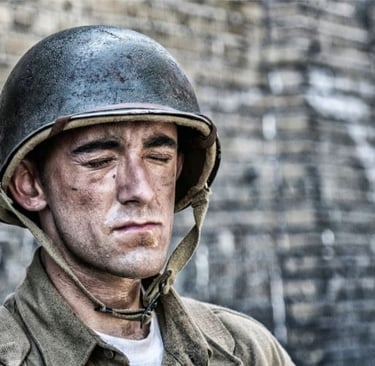 A weary WWII soldier with a dirt-smudged face wearing a steel combat helmet and uniform.