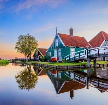 Traditional green Dutch houses reflecting in a calm canal at sunset in Zaanse Schans village.