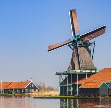 Historic Dutch windmill and wooden houses by the water at Zaanse Schans under a clear blue sky.