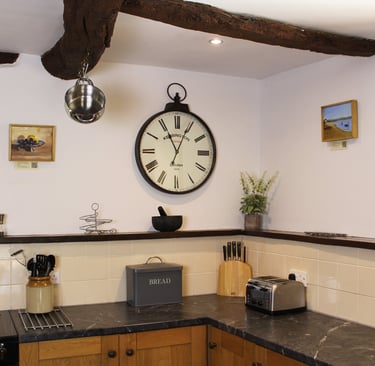 Rustic kitchen interior featuring exposed ceiling beams, a large wall clock, and grey marble countertops.