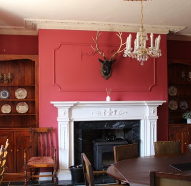 Elegant red dining room featuring a white mantel fireplace, deer head mount, and antique wooden hutches.