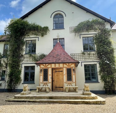 Traditional English manor house with a timber-framed porch, stone lion statues, and climbing ivy.