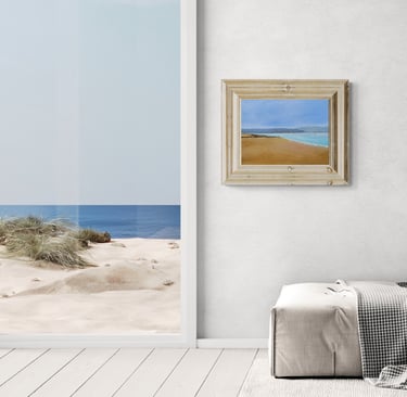 Modern living room with beach wall art and view of sand dunes through a large window.