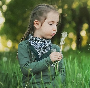 a little girl sitting in the grass with a dandelion