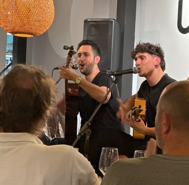Two male musicians singing and playing SPAN guitars during a live performance at a restaurant venue.