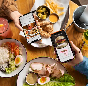 a person holding a cell phone phone in front of a table with food and drinks