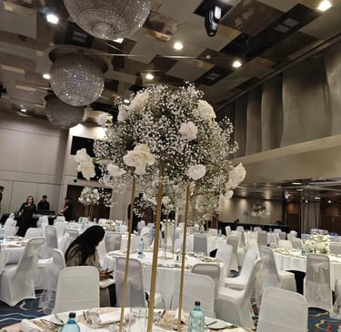 Elegant banquet hall set for an event with white table settings and a large baby's breath floral centerpiece on a gold stand
