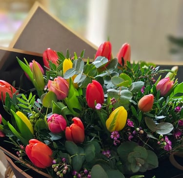 A vibrant bouquet featuring red, yellow, and pink tulips mixed with eucalyptus leaves and small purple flowers