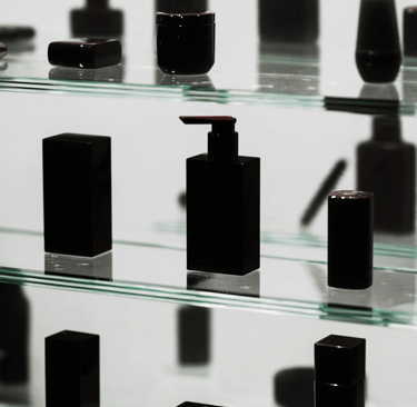 Luxury black cosmetic bottles and jars displayed on tiered glass shelves for skincare packaging.