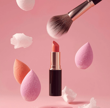 Professional makeup brush, lipstick, and beauty blenders floating over a pink background.
